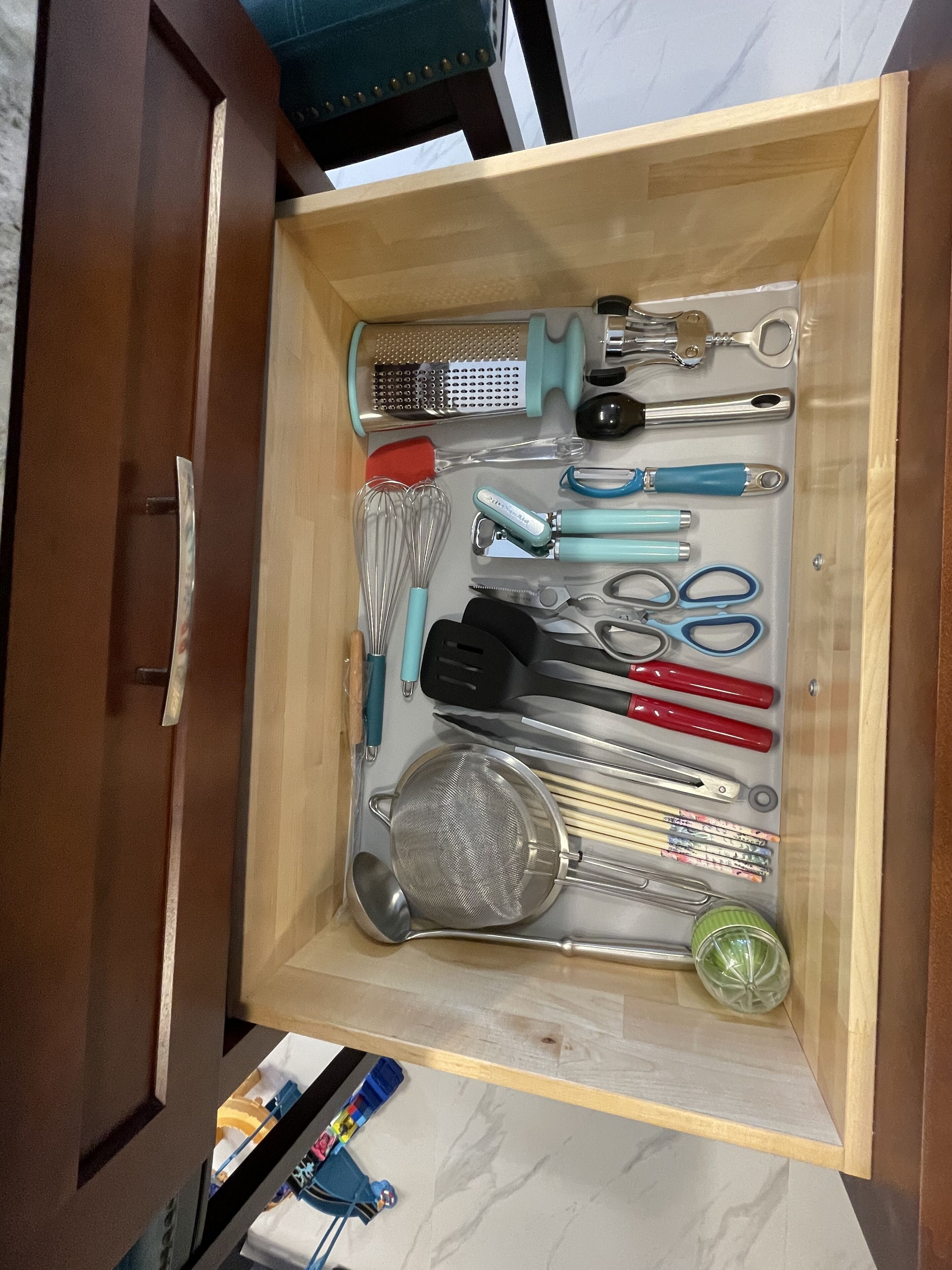 Un cajón con varios utensilios y herramientas de cocina, incluyendo palillos, un rallador y un batidor.
