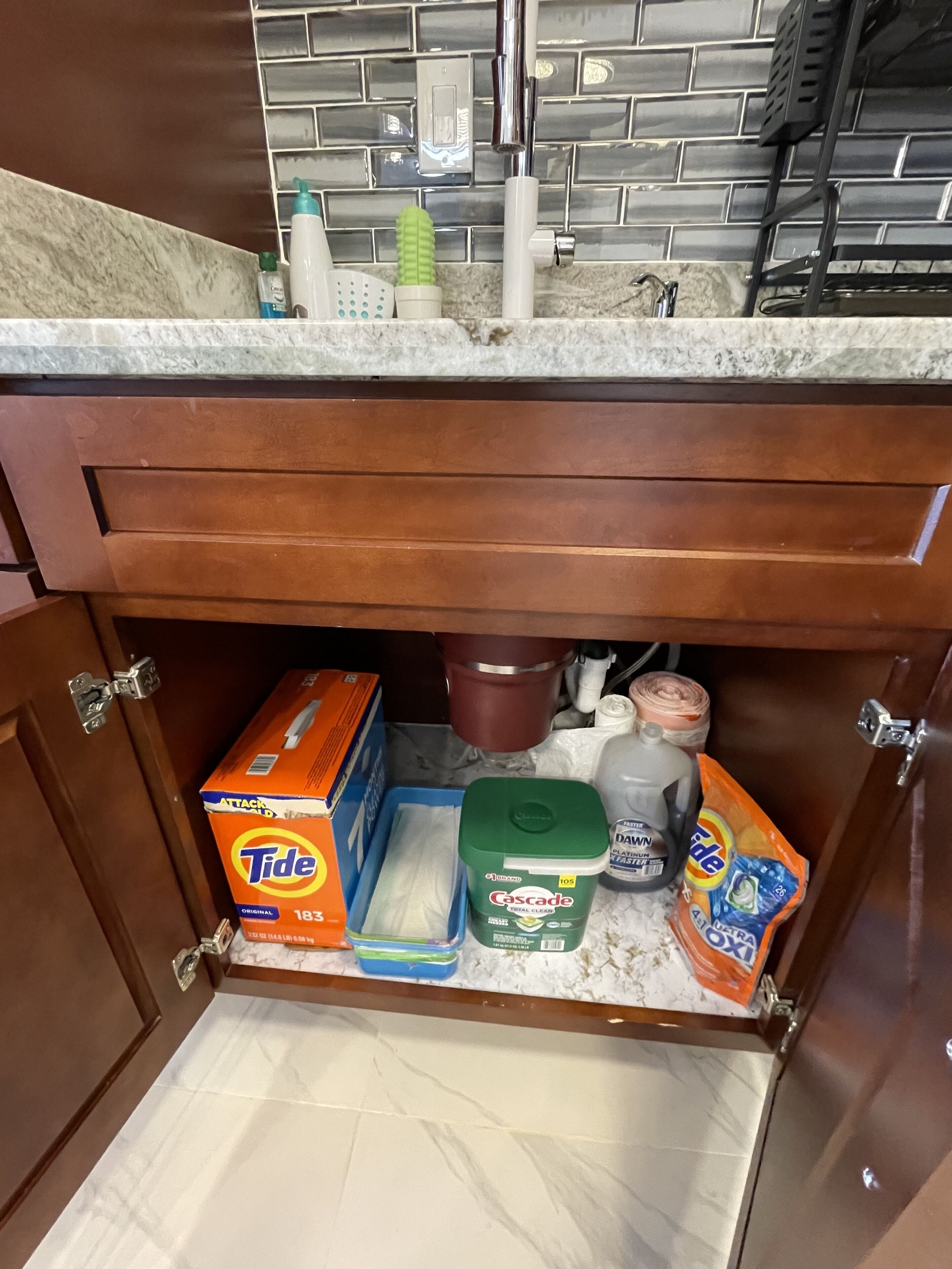 Un armario de cocina con detergente Tide, un recipiente verde y un escurreplatos azul.
