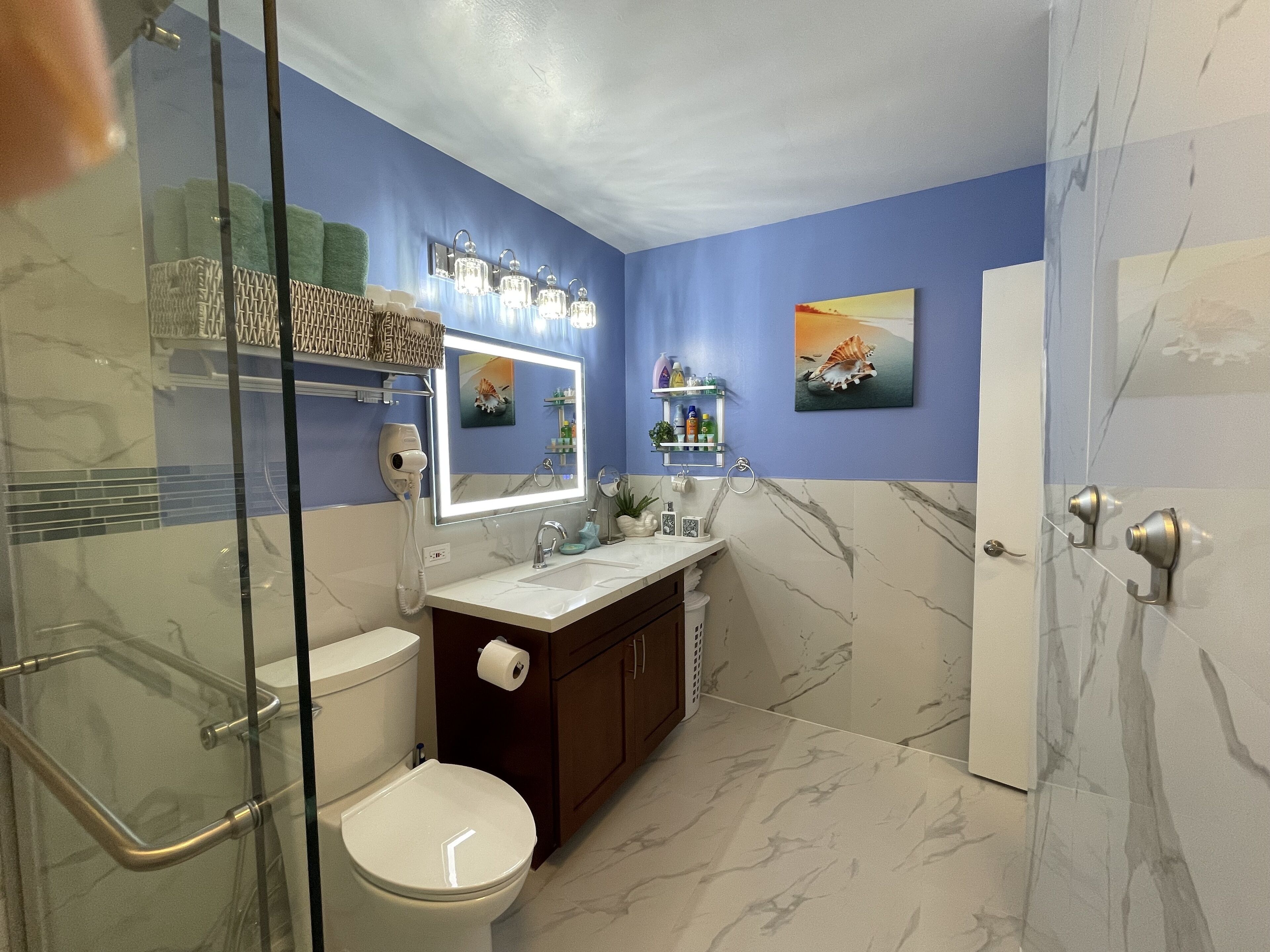 A bathroom with a glass shower enclosure, a white toilet, a marble sink, and a vanity with a mirror.