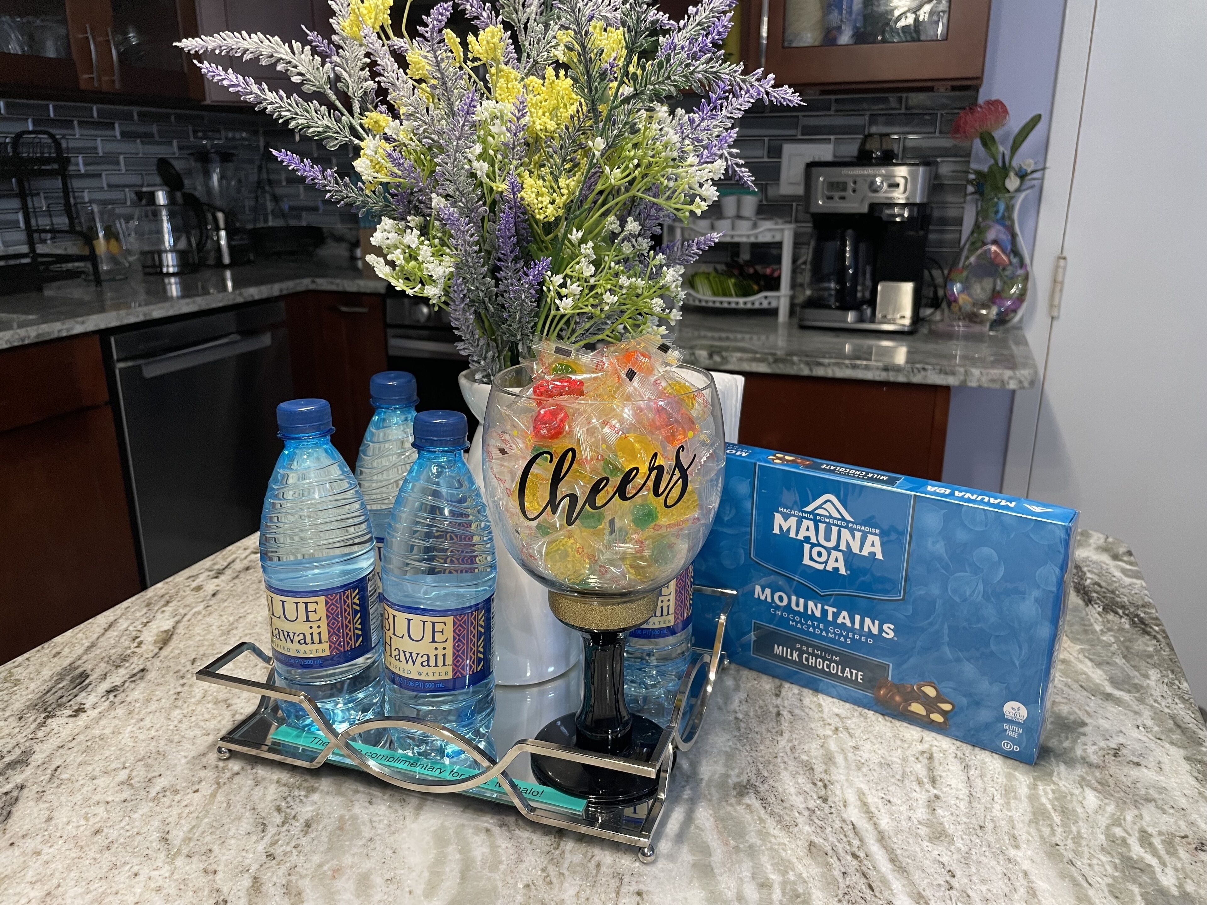 A kitchen counter with a water dispenser, a glass of Cheer candies, and a box of Mauna Loa chocolate.