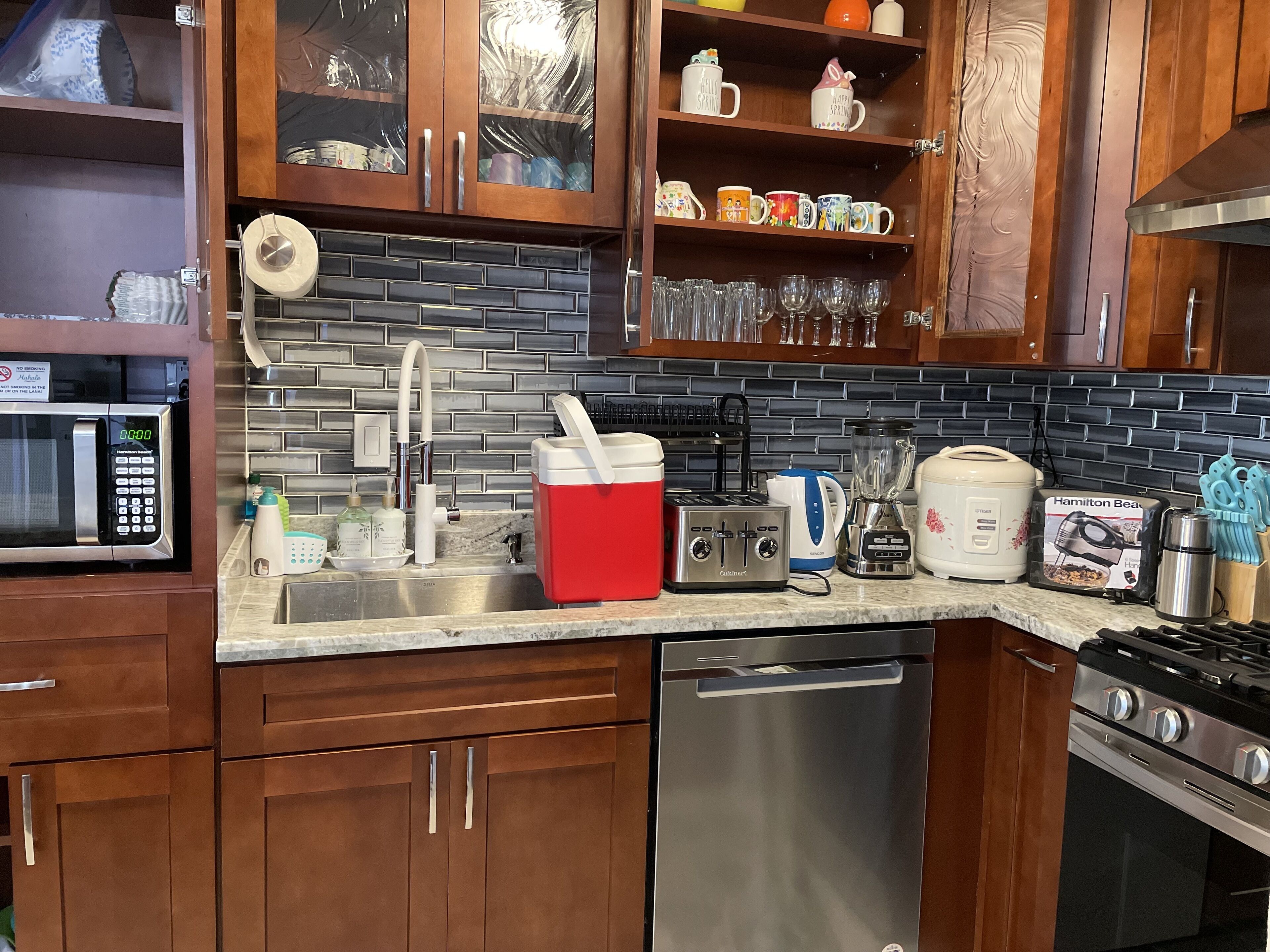 Una cocina moderna con armarios de madera, lavavajillas de acero inoxidable, microondas, tostadora, licuadora y cafetera.