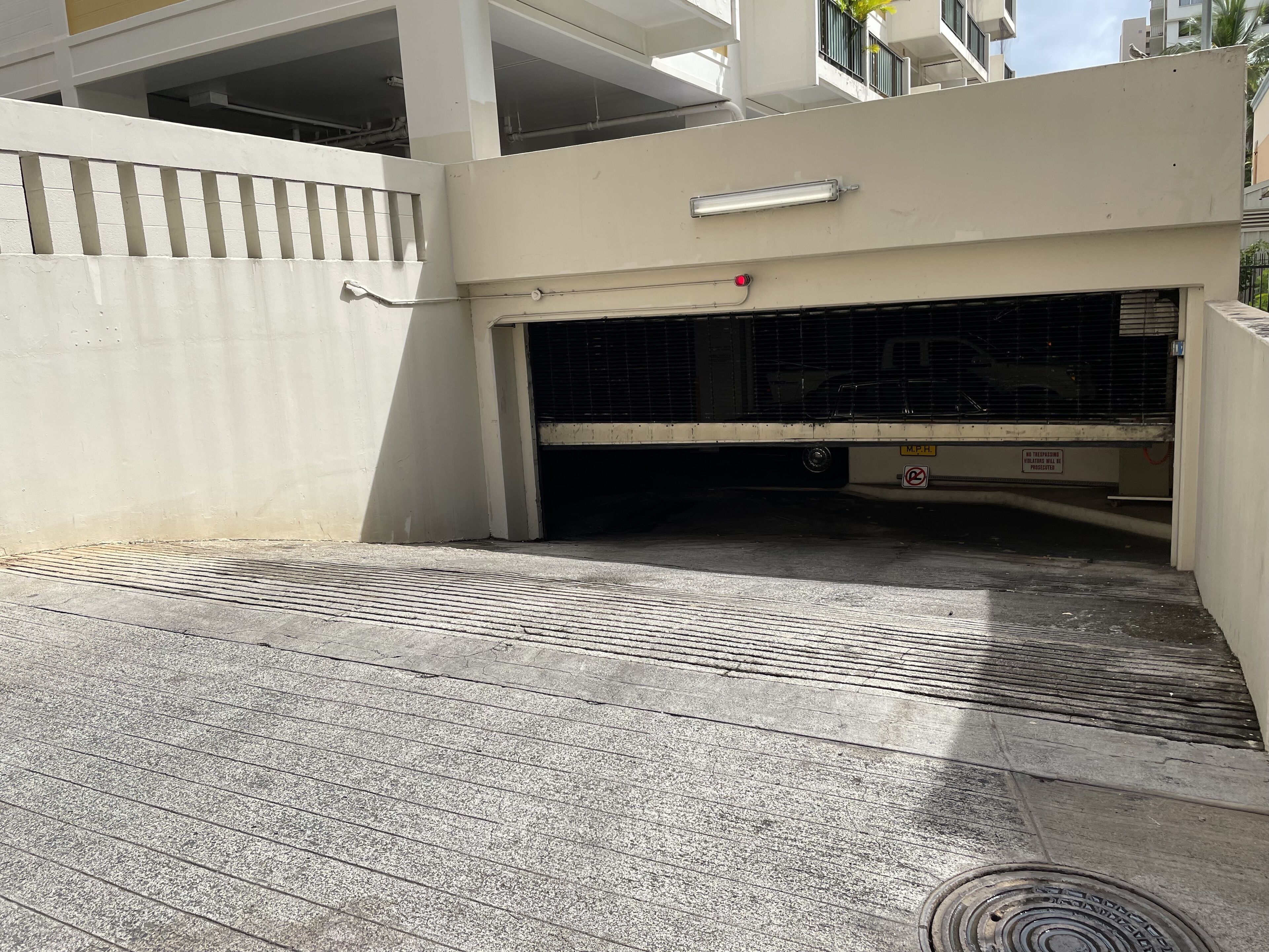 A parking garage entrance with a metal grate, a white wall, and a sign indicating no parking.