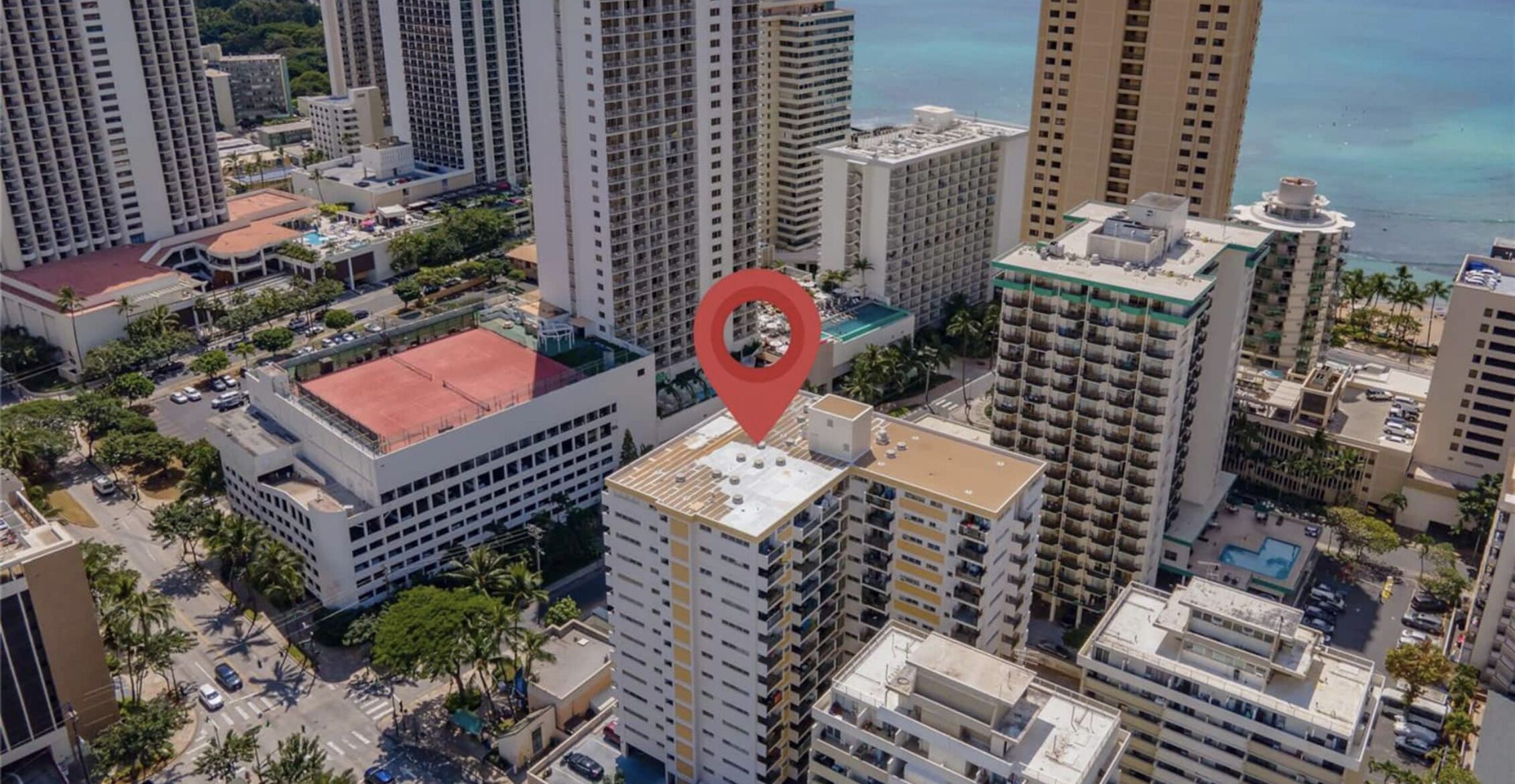 Vista aérea de un complejo de edificios altos con varias construcciones, una estructura de techo rojo y un área de piscina.