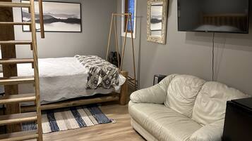 Un lit superposé avec une échelle en bois, un canapé blanc, un téléviseur et des tableaux encadrés au mur.