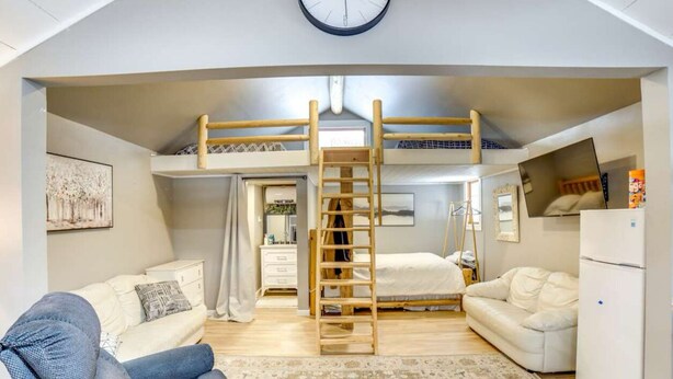 Un dormitorio tipo loft con una cama litera, una escalera, un sofá blanco, un escritorio pequeño y un reloj en la pared.