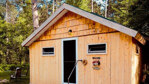 Una cabaña de madera con un cartel de bienvenida, un pequeño porche y un felpudo estampado al frente.