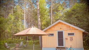 Una cabaña de madera con una mesa y sillas de picnic, rodeada de árboles.