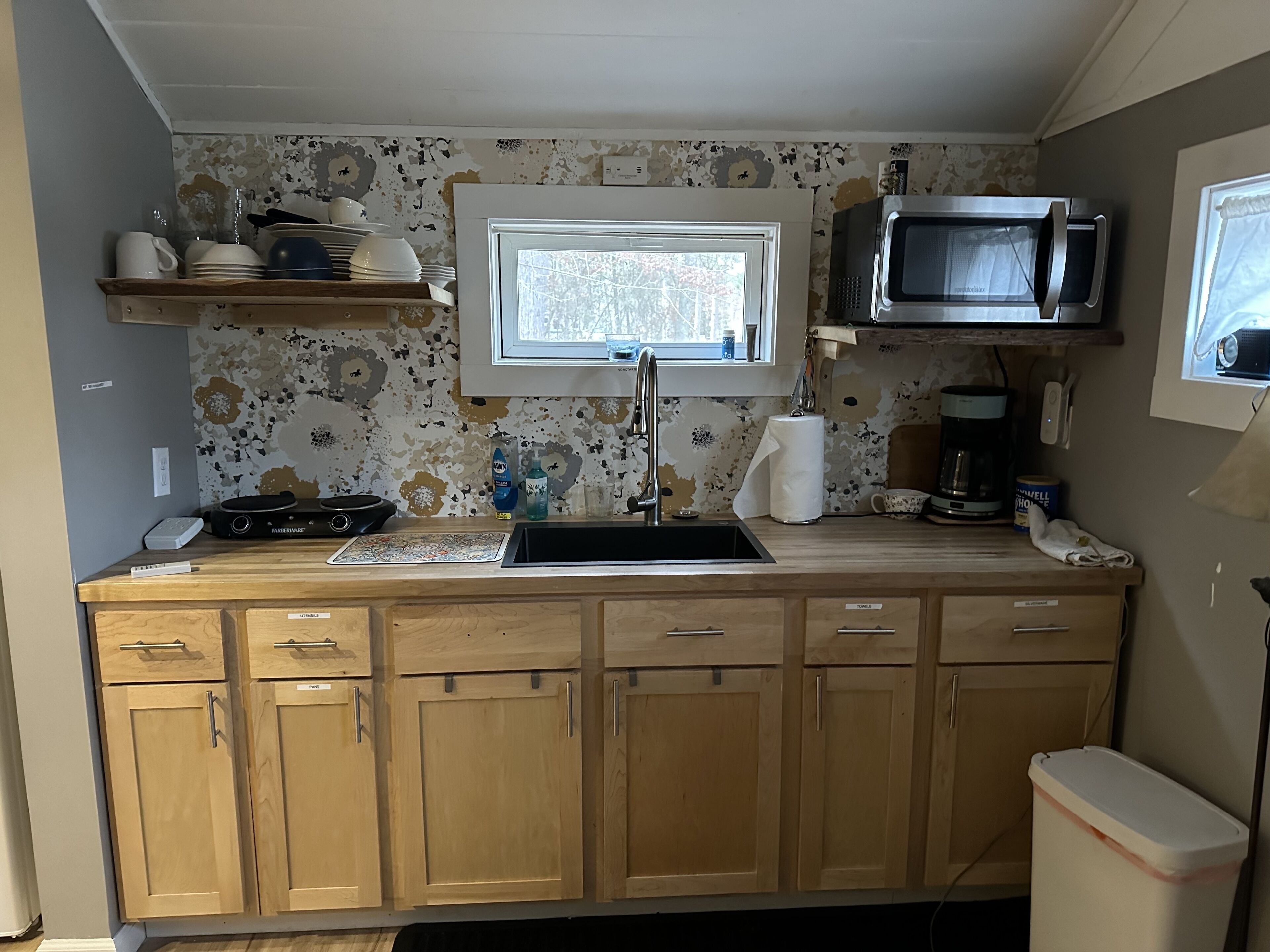 Cocina compacta con gabinetes de madera, microondas integrado, ventana sobre el lavamanos y cafetera.