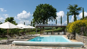 Ein Swimmingpool mit Liegestühlen und Sonnenschirmen, umgeben von Steinböden und viel Grün.