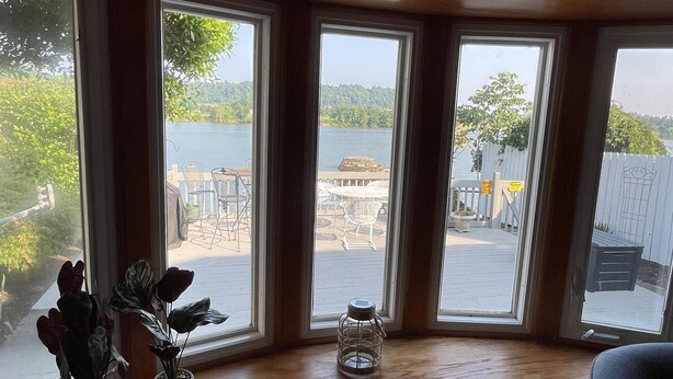 A room with a large window overlooking a dock and water, a small table, and two potted plants.