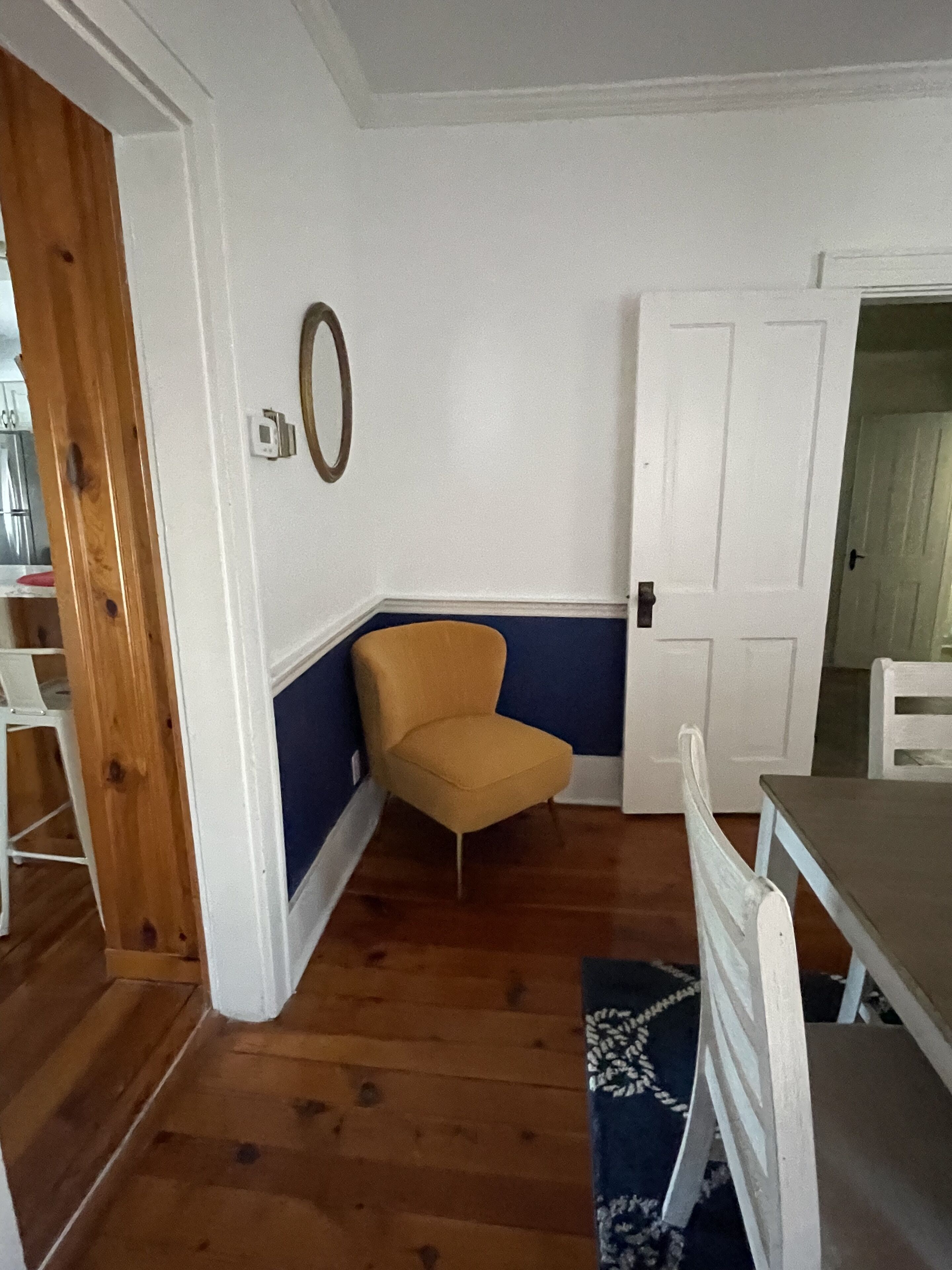Une pièce avec un plancher en bois, une chaise jaune, une porte blanche et une table blanche.