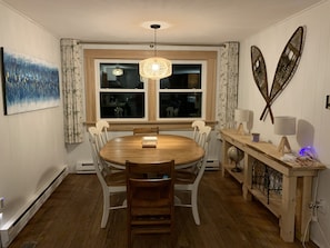 Un espace repas comprenant une table ronde en bois, des chaises blanches, un lustre et des œuvres d’art décoratives accrochées au mur.