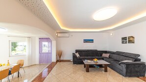 Un salon moderne avec un canapé d’angle gris foncé, une table basse en bois et un coin repas comprenant une table et des chaises.