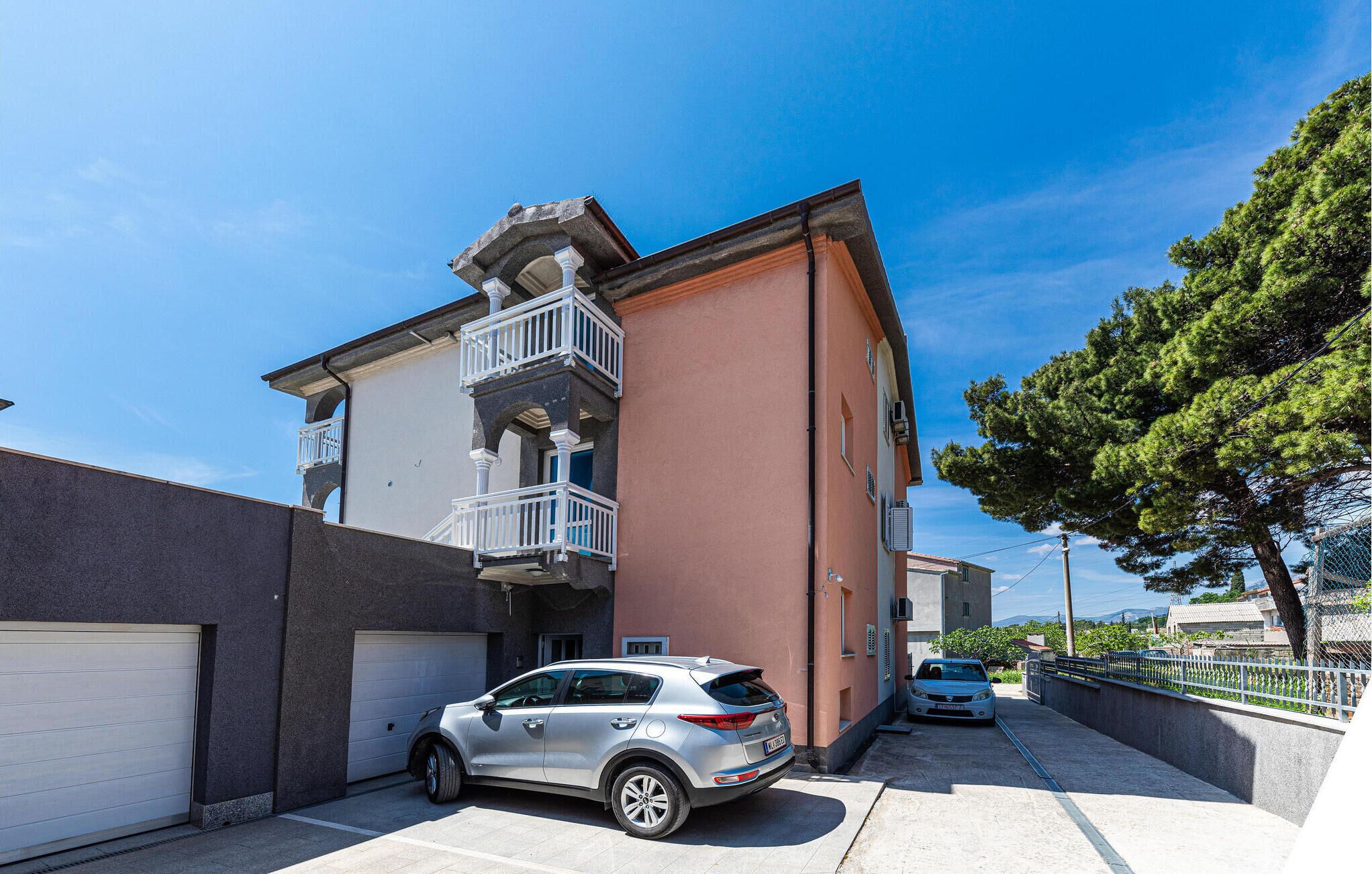 A multi-story building with a garage, a car parked in front, and a tree to the right.