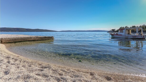 Une plage dégagée avec une eau calme, un bateau amarré sur la droite et une côte lointaine.