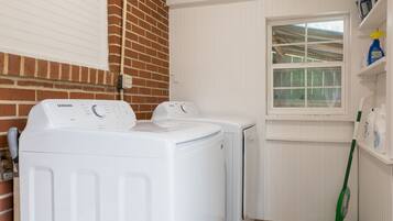 A laundry room with two white front-loading washing machines, a window, and a green mop leaning against the wall.