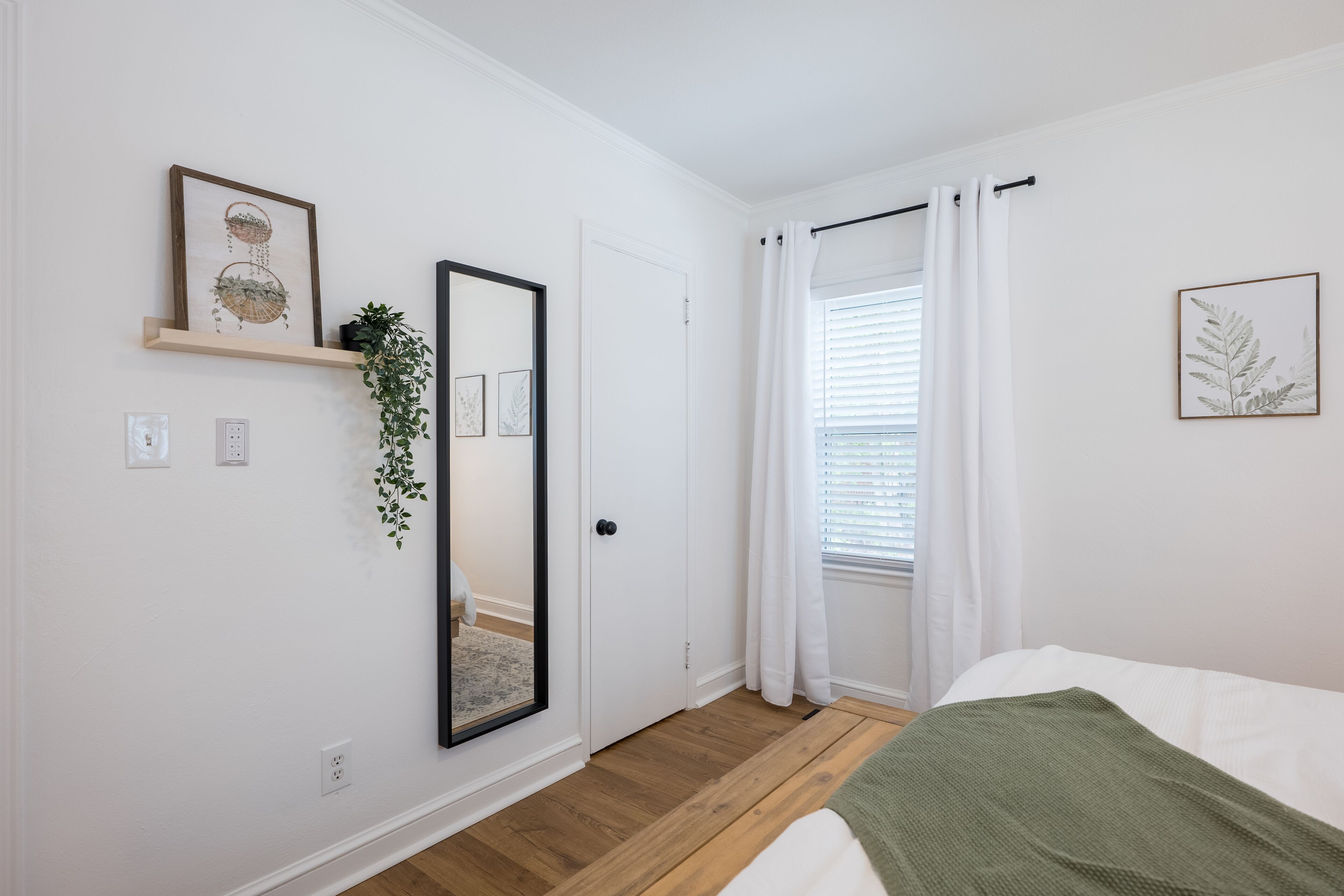 A bedroom with a bed, a mirror, a door, and a window with curtains.