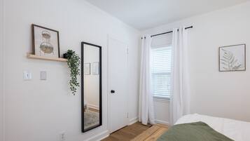 A bedroom with a bed, a mirror, a door, and a window with curtains.