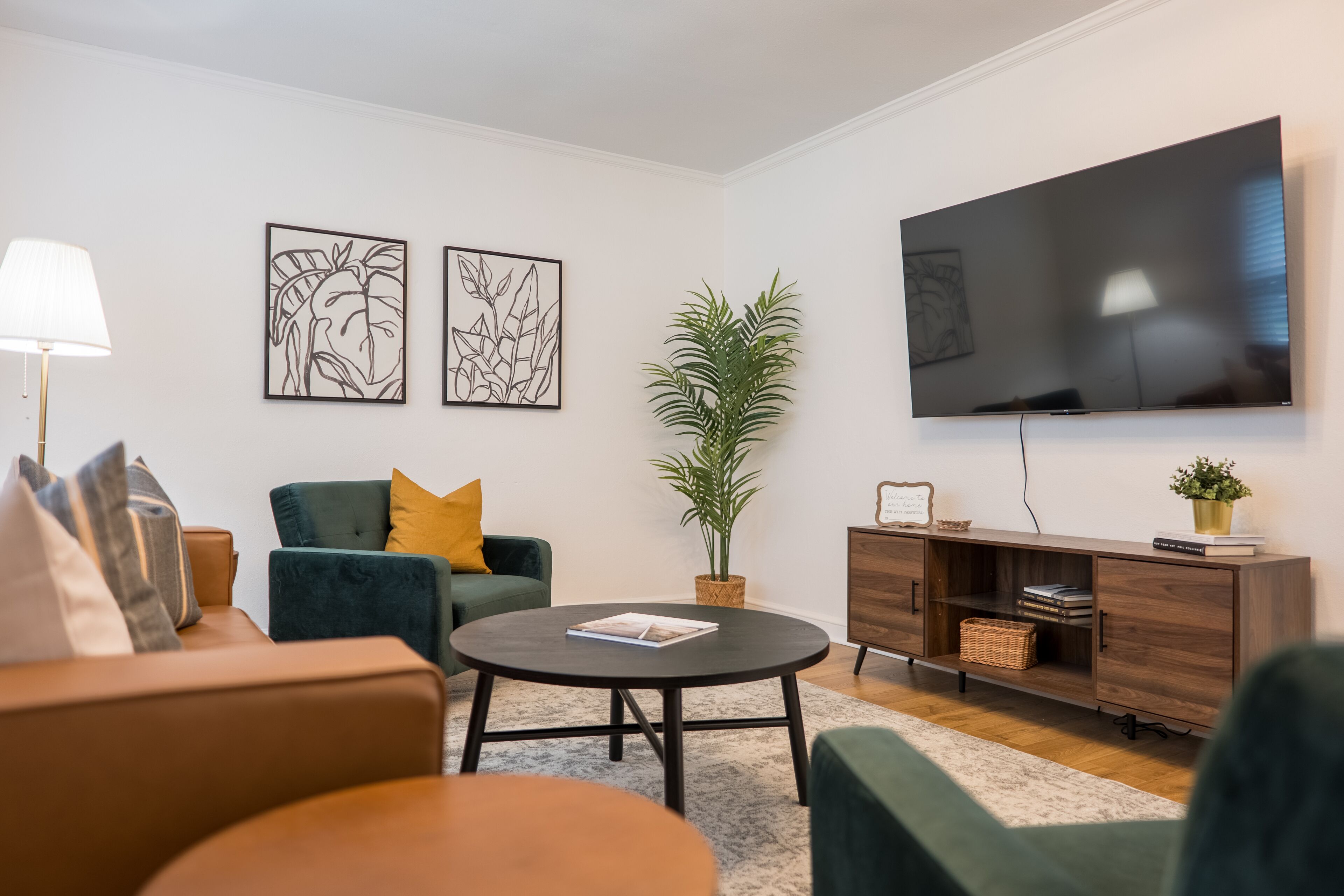 Een moderne woonkamer met een bank, fauteuil, salontafel en een aan de muur bevestigde televisie.