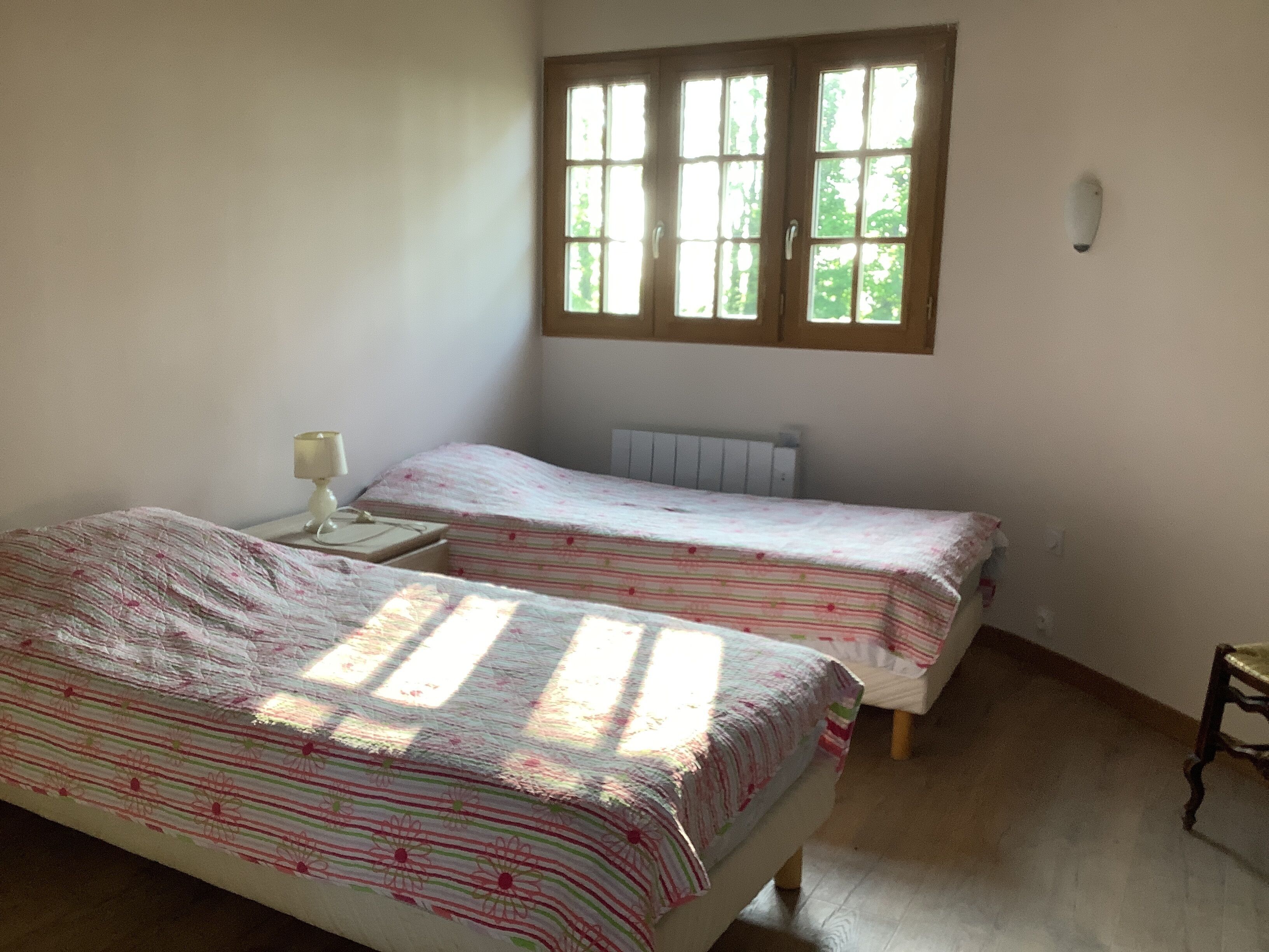 A bedroom with two single beds, a nightstand with a lamp, and a window with blinds.