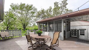 Eine überdachte Terrasse im Freien mit einem runden Tisch und Stühlen, umgeben von einer Holzterrasse und einem weißen Zaun.
