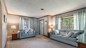 Ein gemütliches Wohnzimmer mit zwei grauen Sofas, einem Holztisch und einer Tür mit Fenster.