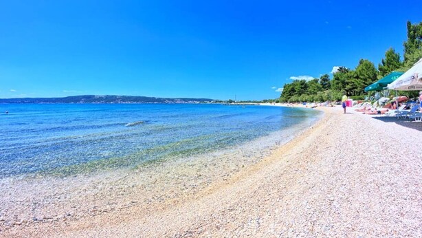 A beach with clear water, pebbles, and umbrellas. - Brand new design apartment with big terrace (Kaštel Štafilić)