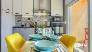 A modern kitchen with white cabinets, a stainless steel range hood, and a dining area with yellow chairs and blue plates. - Brand new design apartment with big terrace (Kaštel Štafilić)