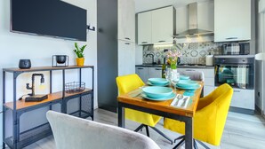 A modern kitchen with white cabinets, a dining table with yellow chairs, and a TV mounted on the wall. - Brand new design apartment with big terrace (Kaštel Štafilić)