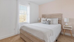 A bedroom with a wooden bed, white bedding, two bedside tables with lamps, and a window with blinds.