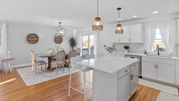 A modern kitchen with white cabinetry, a central island, pendant lights, and a view to the outside.
