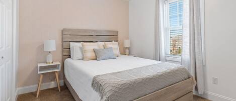 Een slaapkamer met een houten hoofdeinde, een bed met witte lakens, twee nachtkastjes met lampen en een raam met gordijnen.