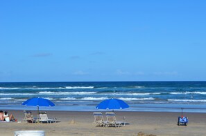A beach with two blue umbrellas, two lounge chairs, and a beach cart. - Coastal Island Retreat! Right off the beach! (South Padre Island)