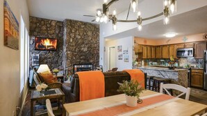 Una sala acogedora con chimenea, pared de piedra y una mesa de comedor con detalles en naranja.