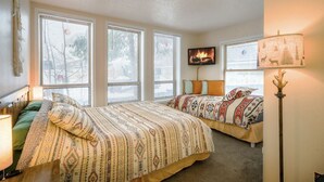 Un dormitorio con dos camas, ventanas amplias, un televisor y una lámpara.