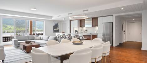 A modern kitchen with a central island, a dining area with a large table and chairs, and a seating area with a sofa and chairs.