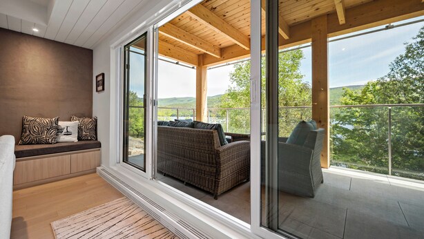 A modern living room with a large sliding glass door leading to an outdoor balcony with a view of the countryside.