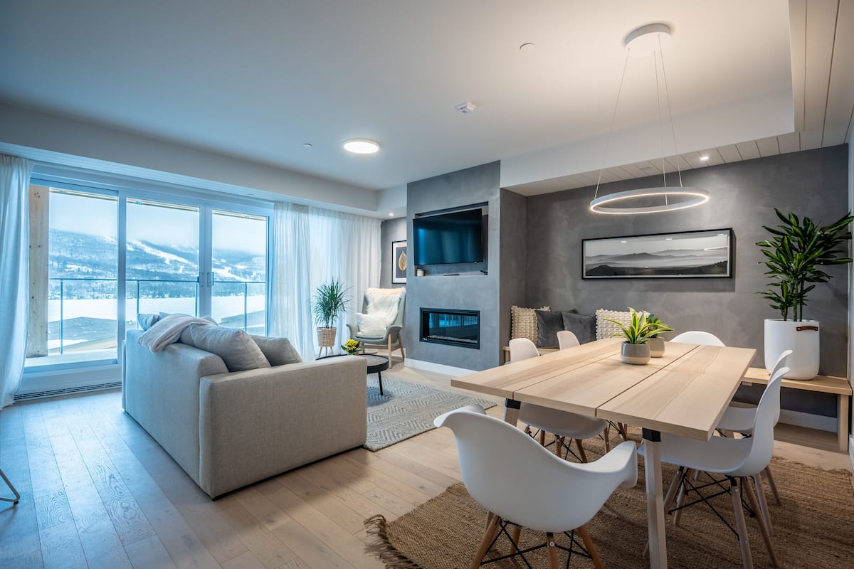 Een moderne woonkamer met een grote houten eettafel, witte stoelen, een bank en een open haard.