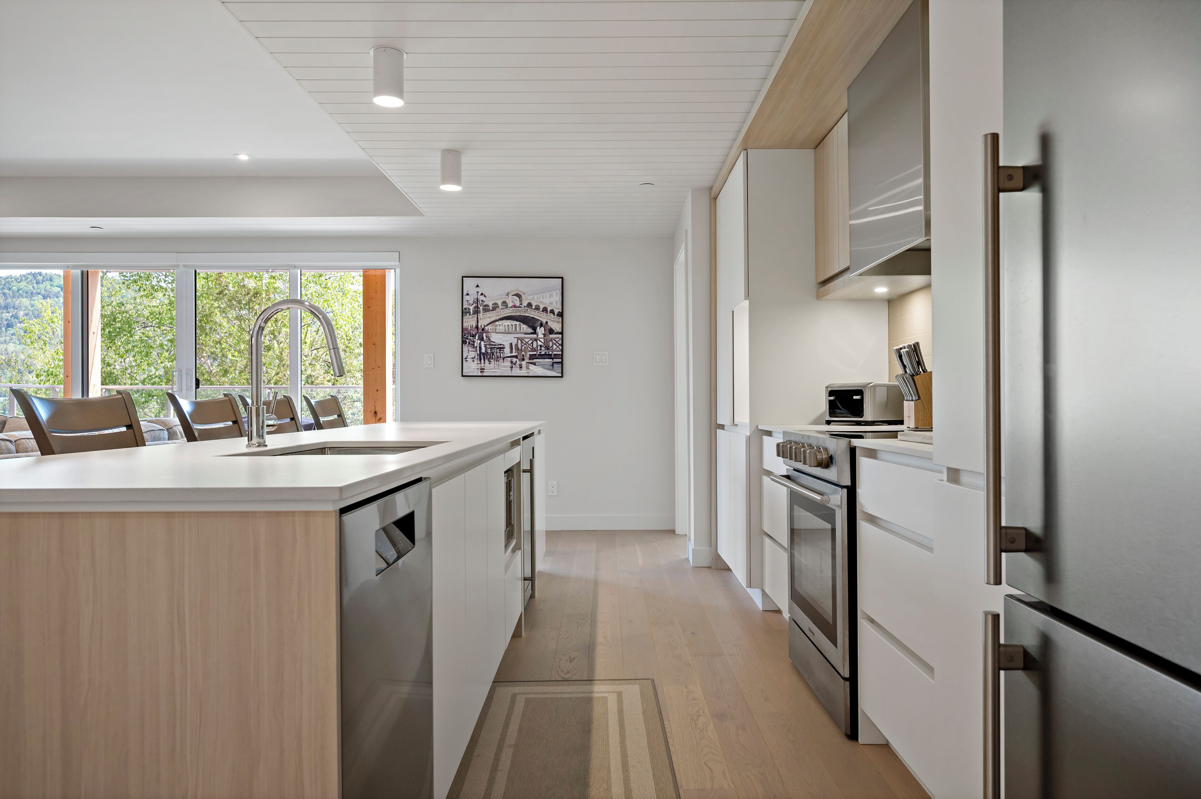 A modern kitchen with a central island, stainless steel appliances, and a large window providing natural light.
