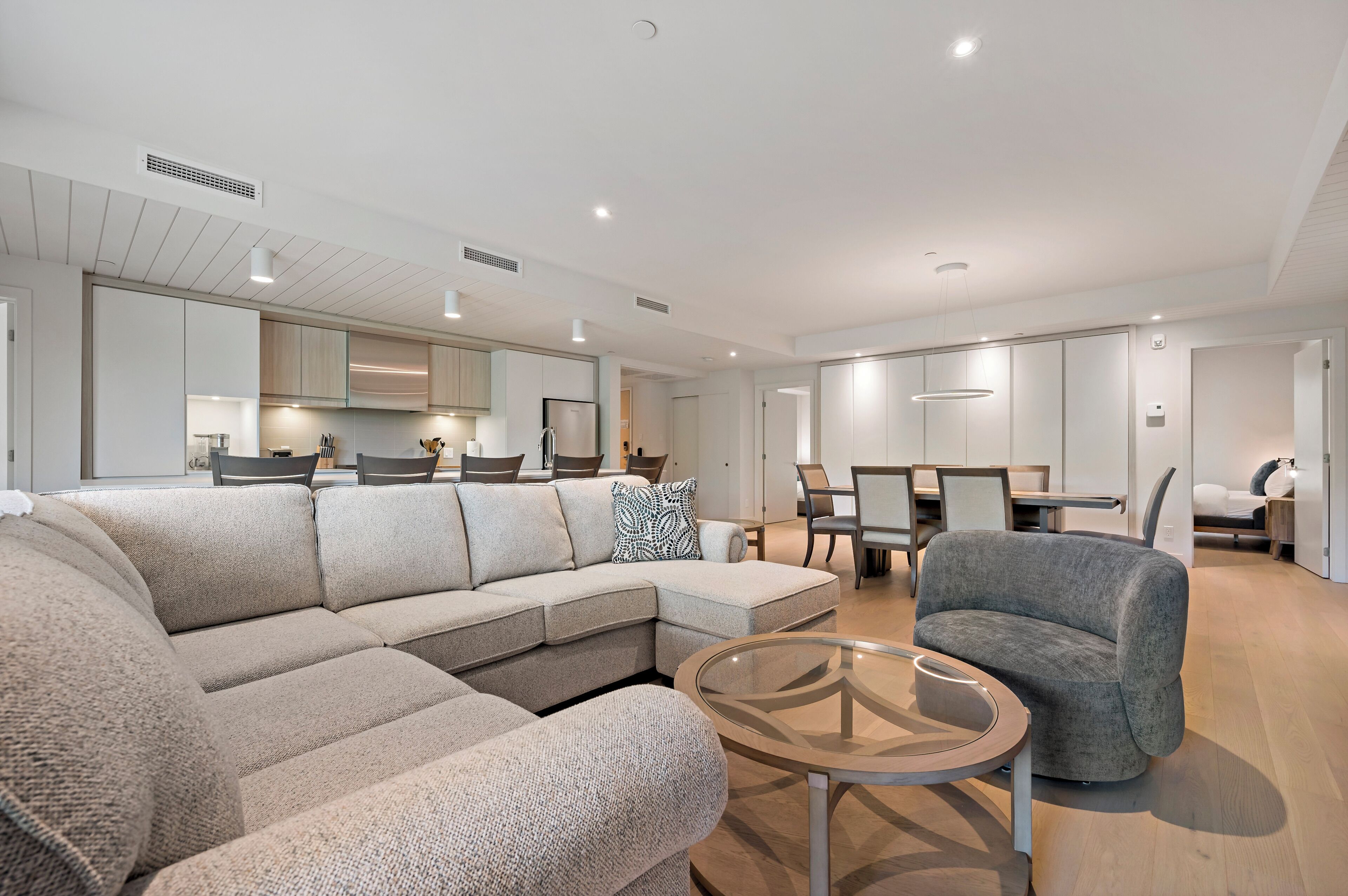 A modern living room with a sectional sofa, a glass coffee table, and a grey armchair.