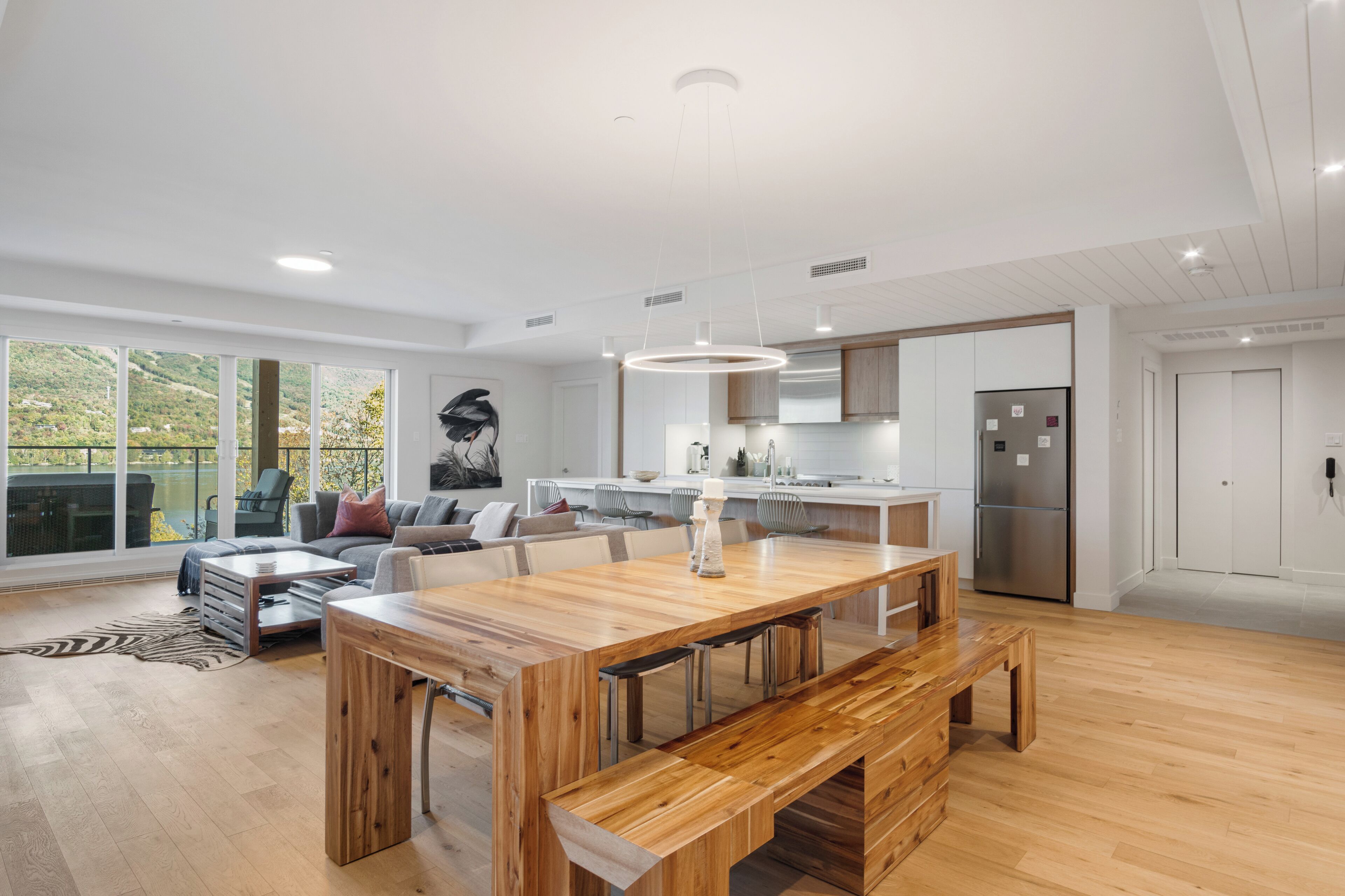 A spacious kitchen with a wooden dining table, modern appliances, and large windows offering a view of the outdoors.