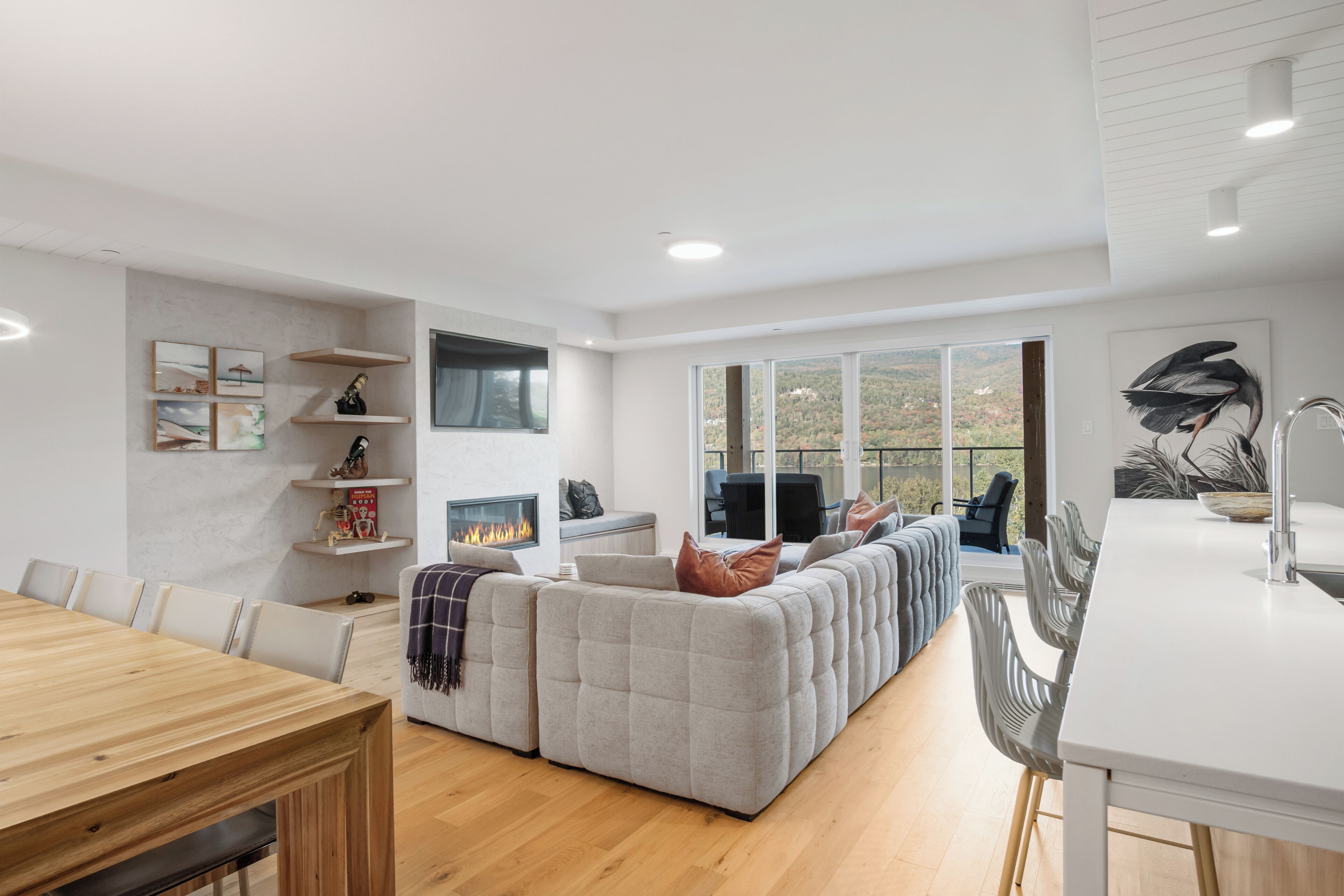 A modern living room with a fireplace, a dining area, and a large window offering a view of the outdoors.