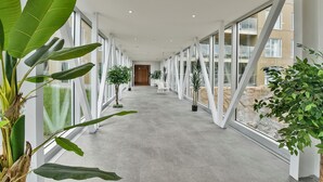 A modern hallway with large windows, potted plants, and a concrete floor.
