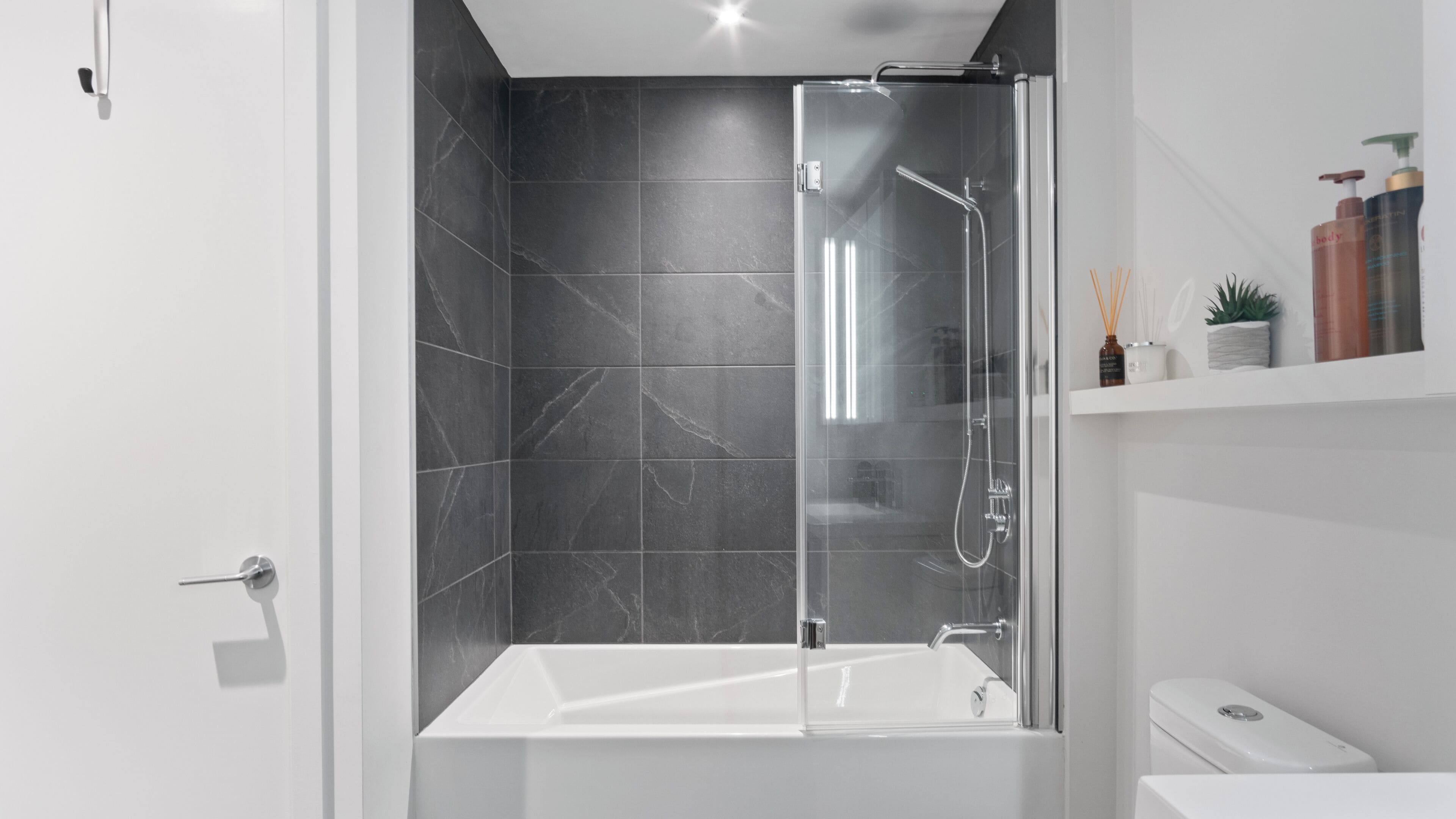 A modern bathroom with a glass-enclosed shower, a white bathtub, and a white toilet.