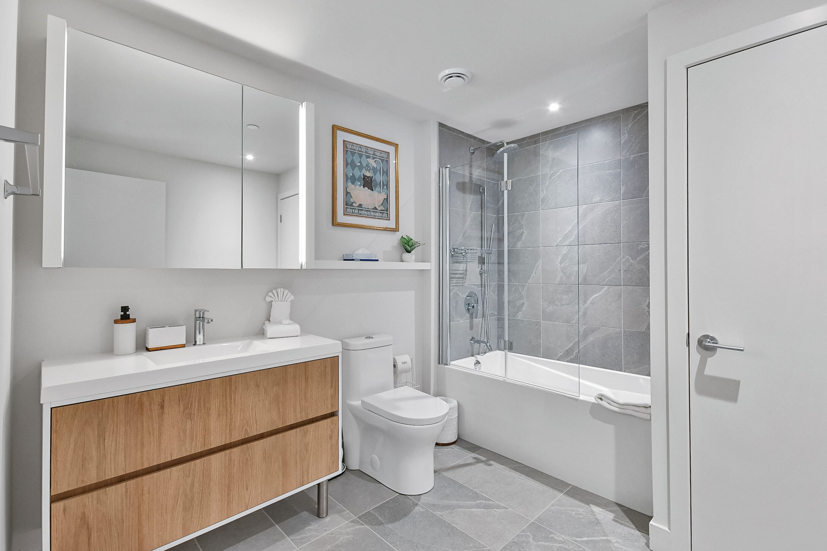 Une salle de bain moderne avec un meuble-lavabo blanc, des toilettes, une douche avec une porte en verre et une baignoire.