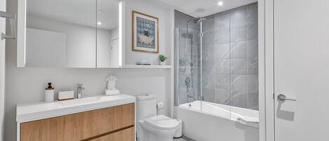 A modern bathroom with a white vanity, a toilet, a shower with a glass door, and a bathtub.