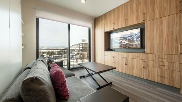 A modern living room with a large window, a sofa, a TV, and wooden cabinets. - Alpine Escape Studio by Park City Vacations (Park City)