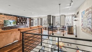 Un vaste espace de vie doté d’un haut plafond, d’un mur décoratif en briques, d’un grand téléviseur et d’un escalier menant à l’étage supérieur.