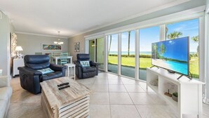 A spacious living room with a large TV, two leather chairs, a coffee table, and a view of the ocean. - Perfect Beachfront Escape at Ocean House 122 (St. Augustine)
