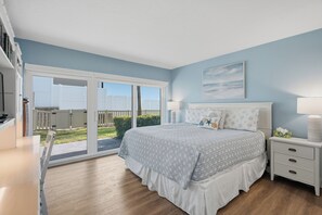 A bedroom with a bed, a nightstand, a window, and a view of the outdoors. - Perfect Beachfront Escape at Ocean House 122 (St. Augustine)